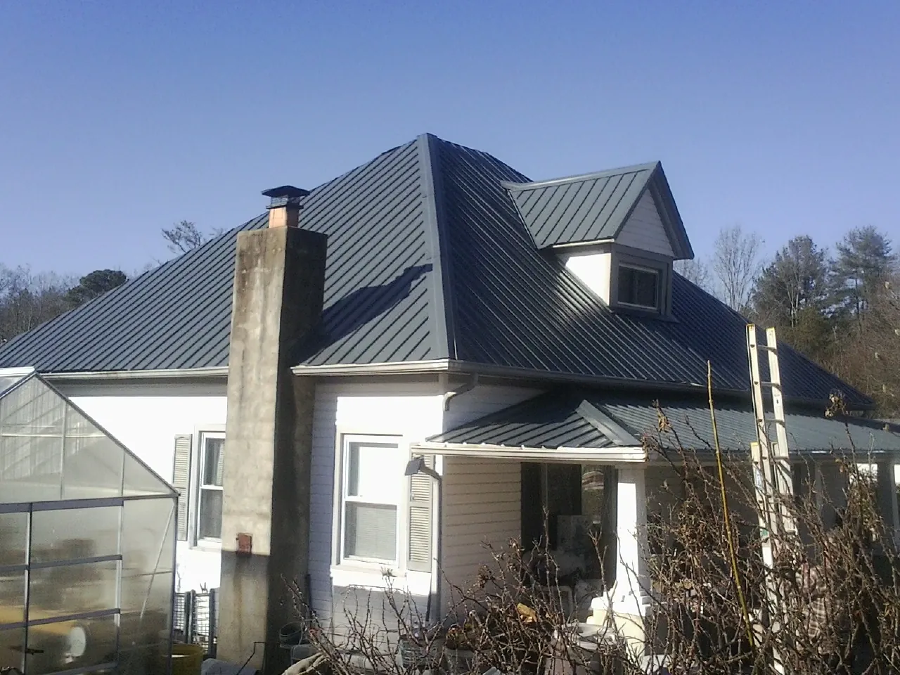 Dark blue standing seam metal roof on a white farmhouse with dormer — Slate & Tile Roof Repair by Roofing Brothers in Lando