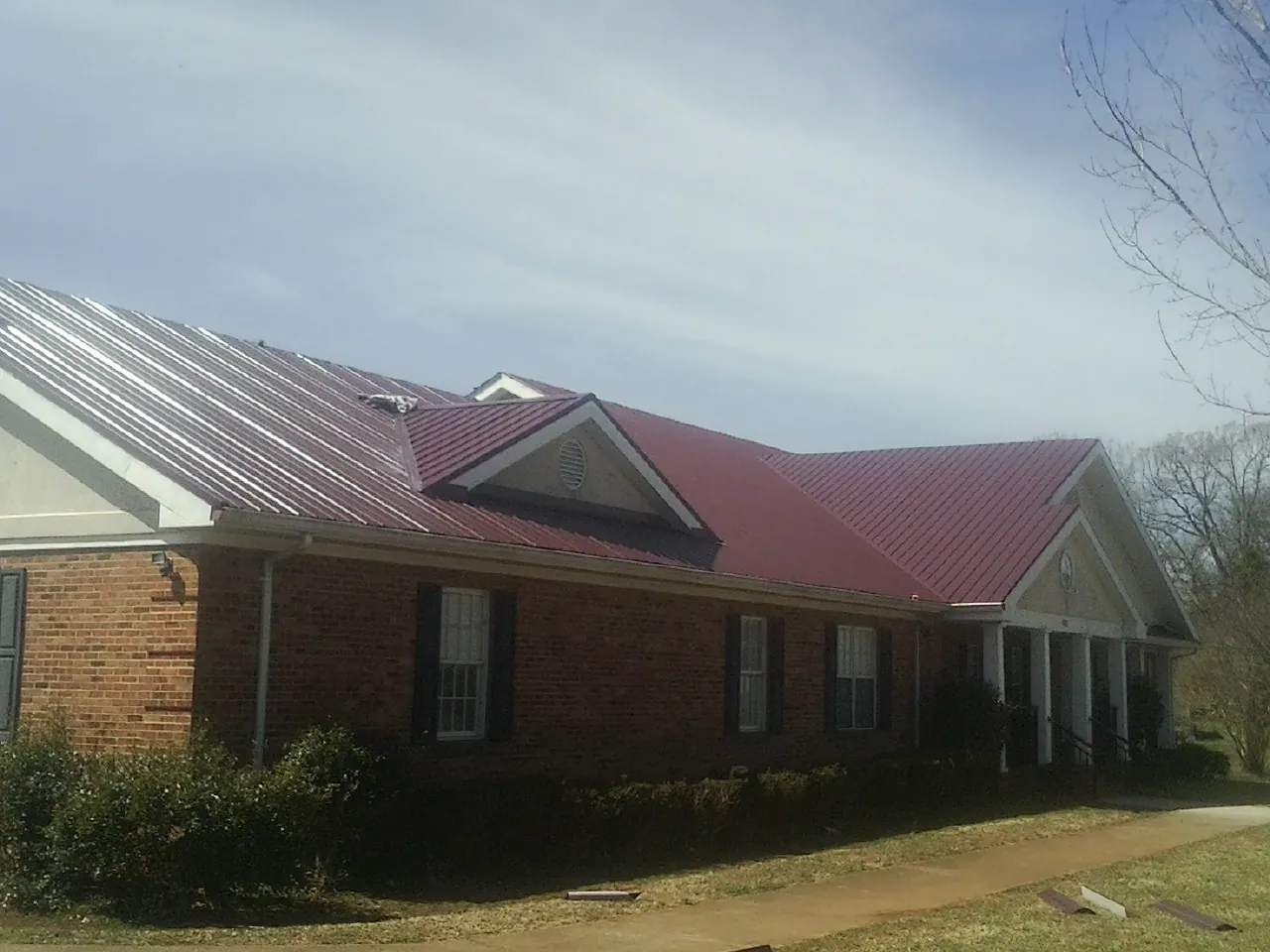 Red metal roof with gabled entries on a long brick building, from a Hail Damage Roof Repair job in Lando
