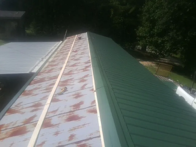 Old rusted panels beside newly installed green metal roofing — Wind Damage Roof Repair by Roofing Brothers in Lando