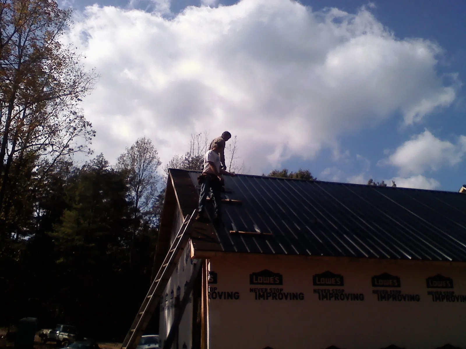 Roofer fastening dark metal panels high against a cloudy sky, from a Roof Inspection job in Lando