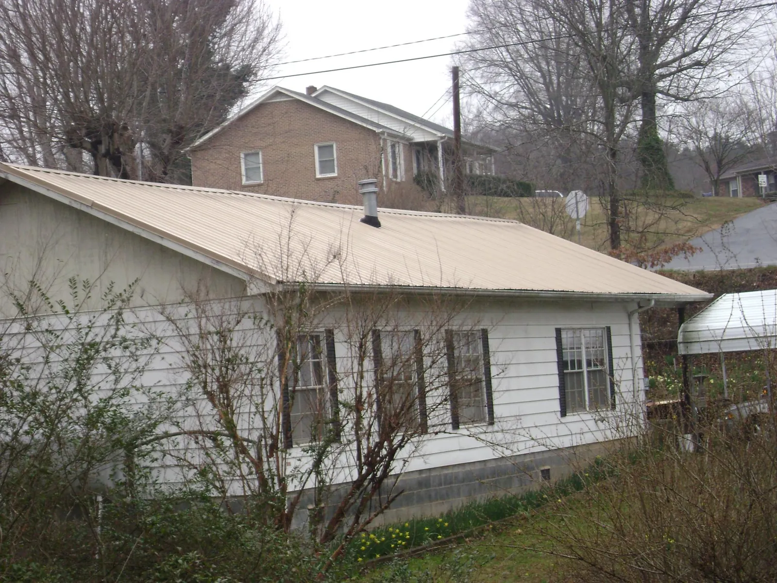 Tan metal roof on a white sided house set into a hillside — Commercial Roofing by Roofing Brothers in Lando