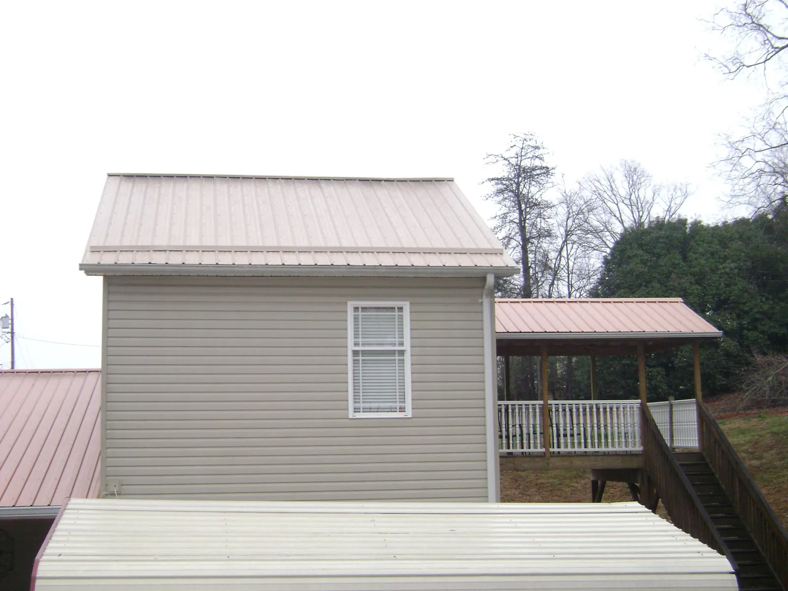 Tan metal roofs on a two story addition and attached porch, from a Roof Replacement job in Lando